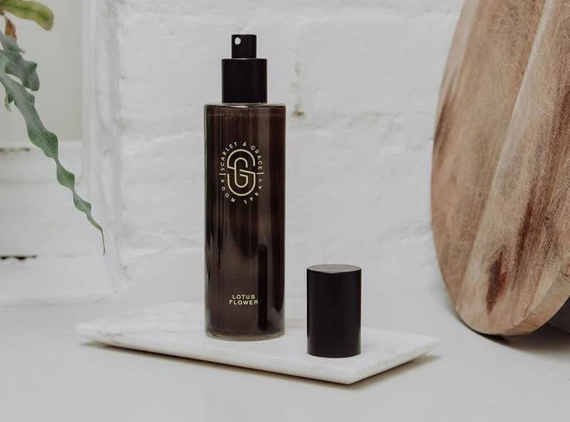 Brown bottle with black cap on a white surface with a wooden object and plant in the background